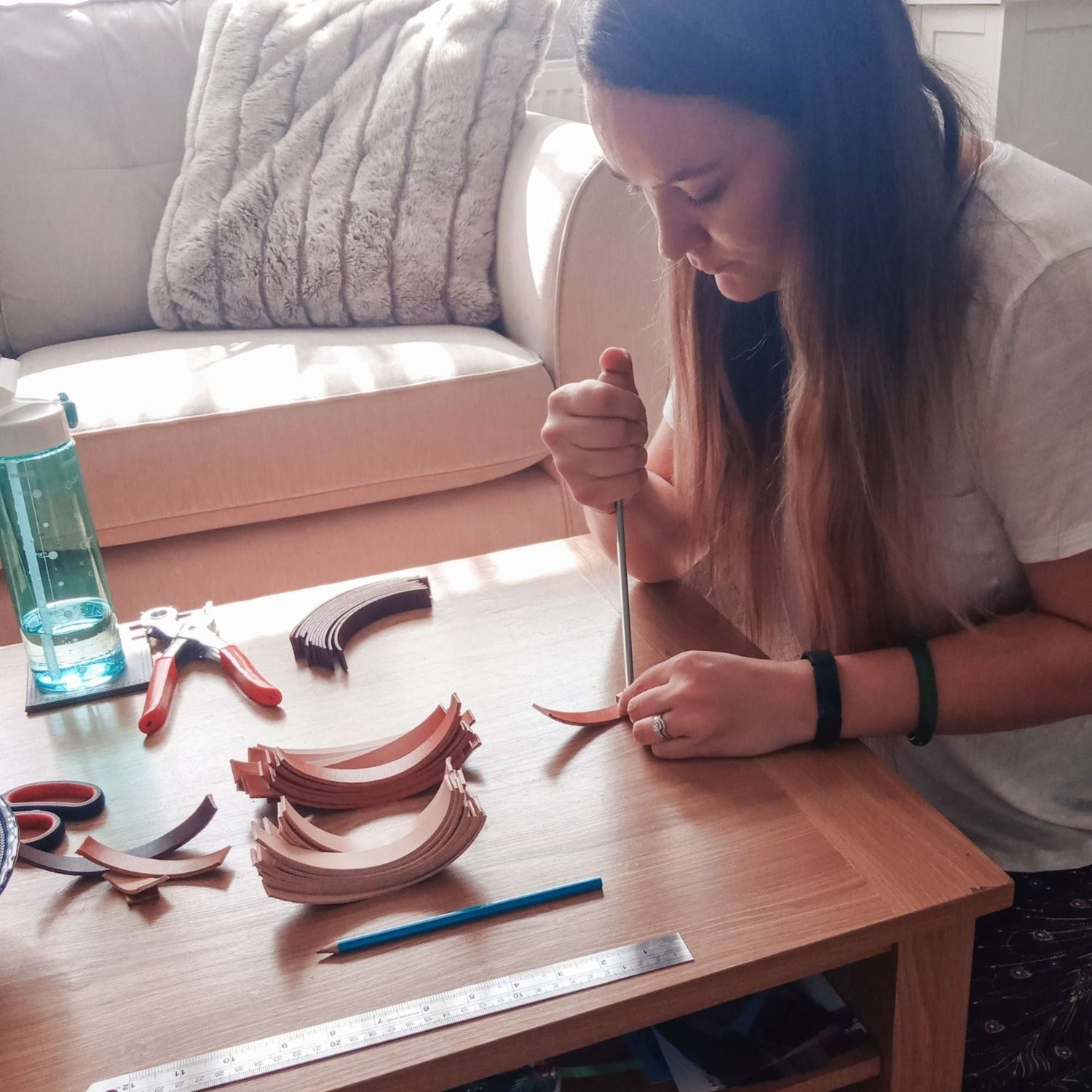 Woman crafting leather keyrings on a wooden table with tools and materials for travel gifts.