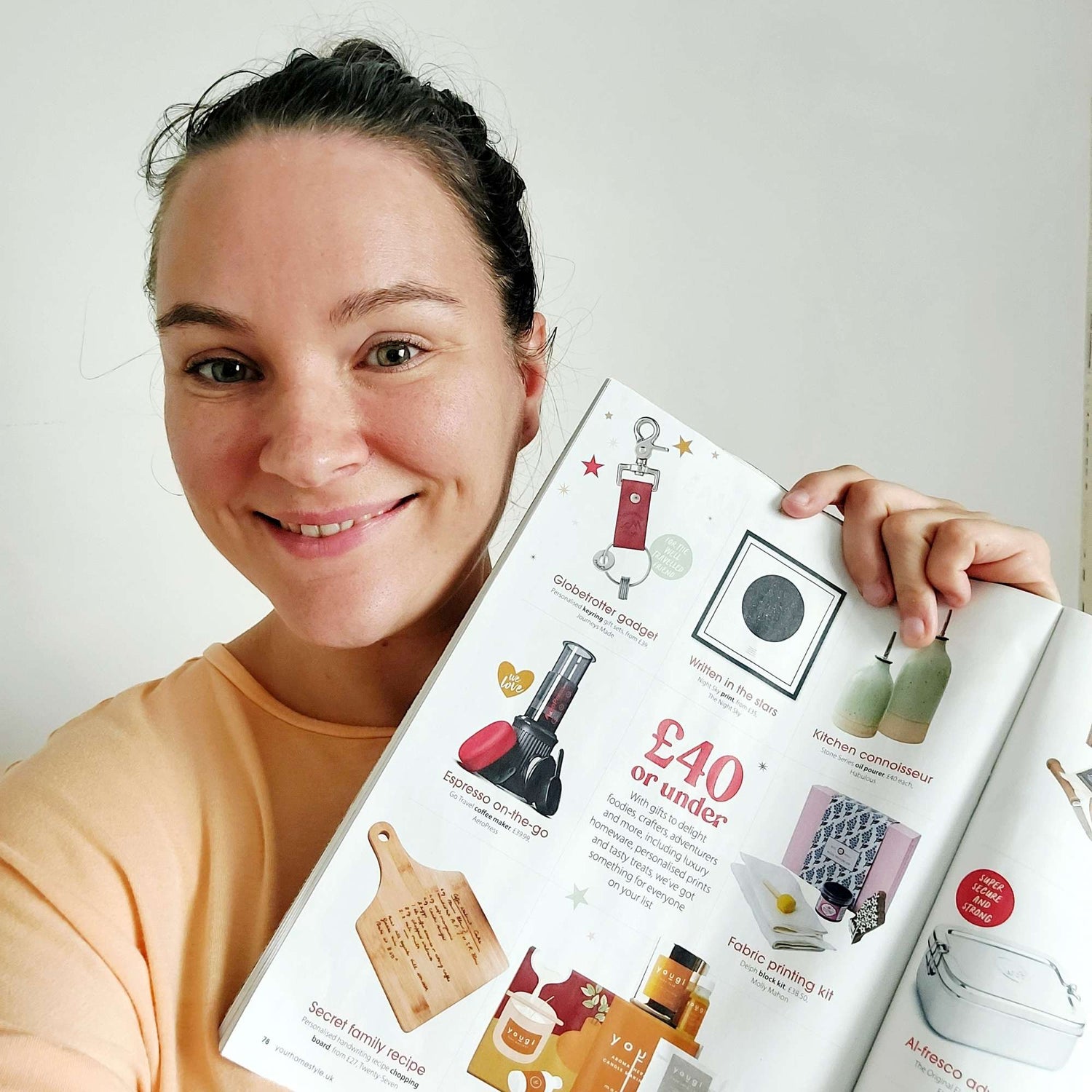 Smiling woman holding a magazine page showcasing various gifts, including a keyring and travel gifts.
