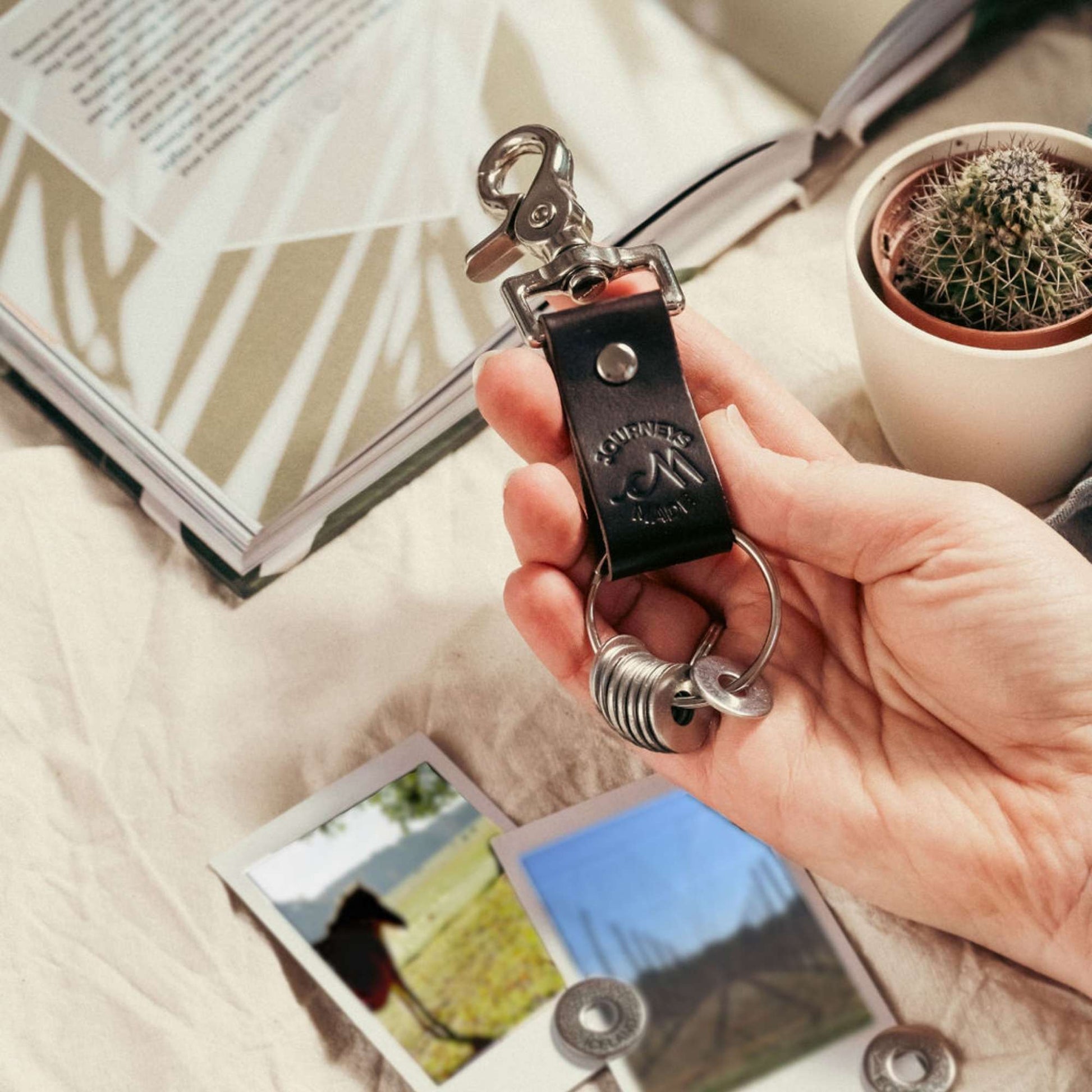 dark brown travel gift consisting of leather travel keyring and engraved travel tokens on the split ring with loose tokens on a table underneath, on the table are polaroid holiday photos