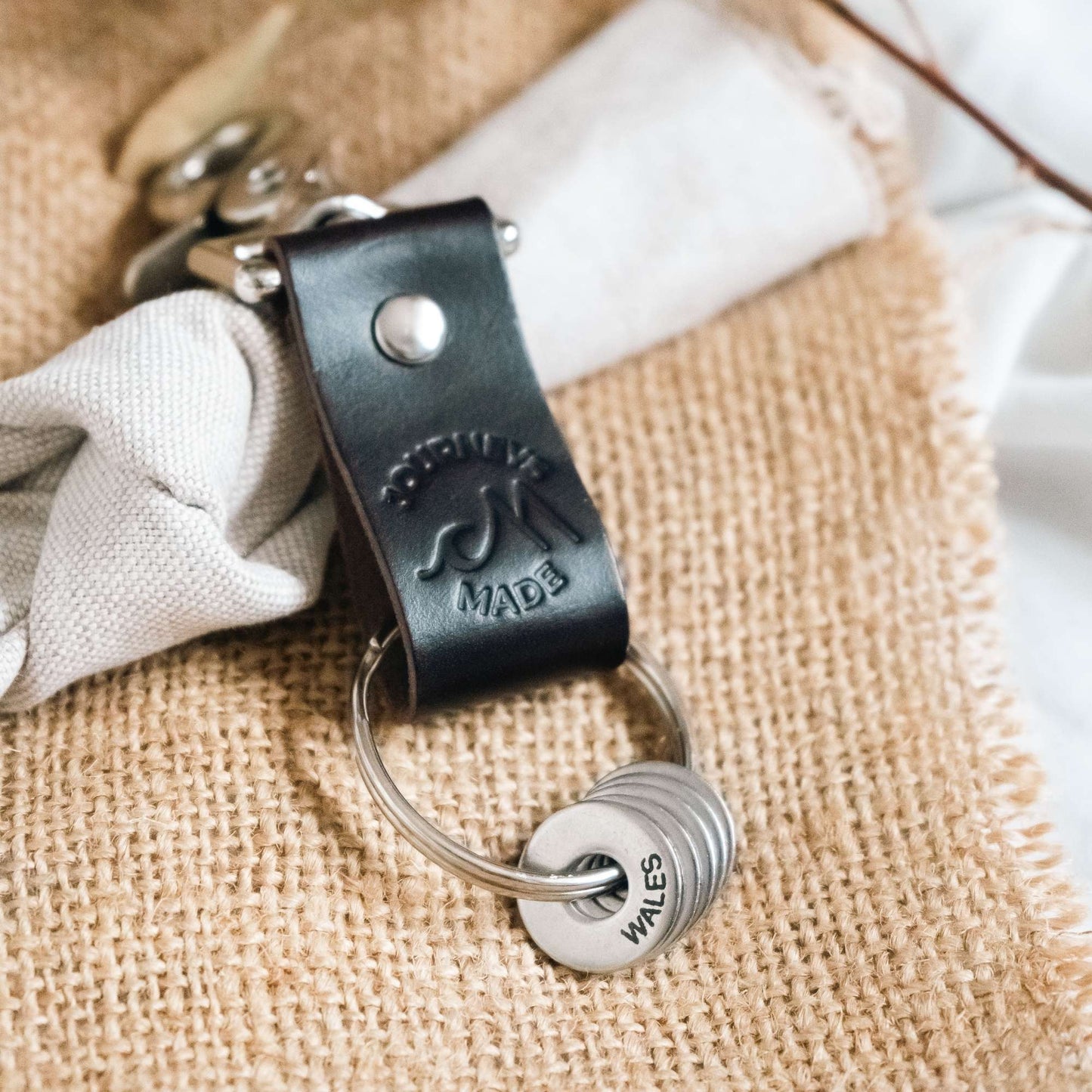 dark brown travel gift consisting of leather travel keyring and engraved travel tokens on the split ring laying on hessian fabric and cream muslin