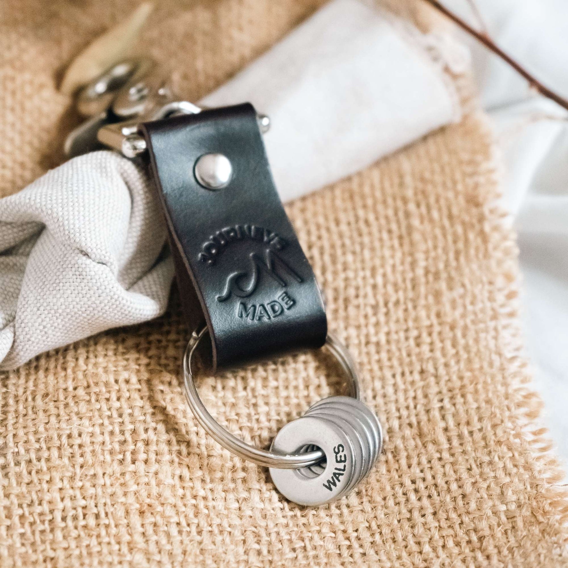 dark brown travel gift consisting of leather travel keyring and engraved travel tokens on the split ring laying on hessian fabric and cream muslin