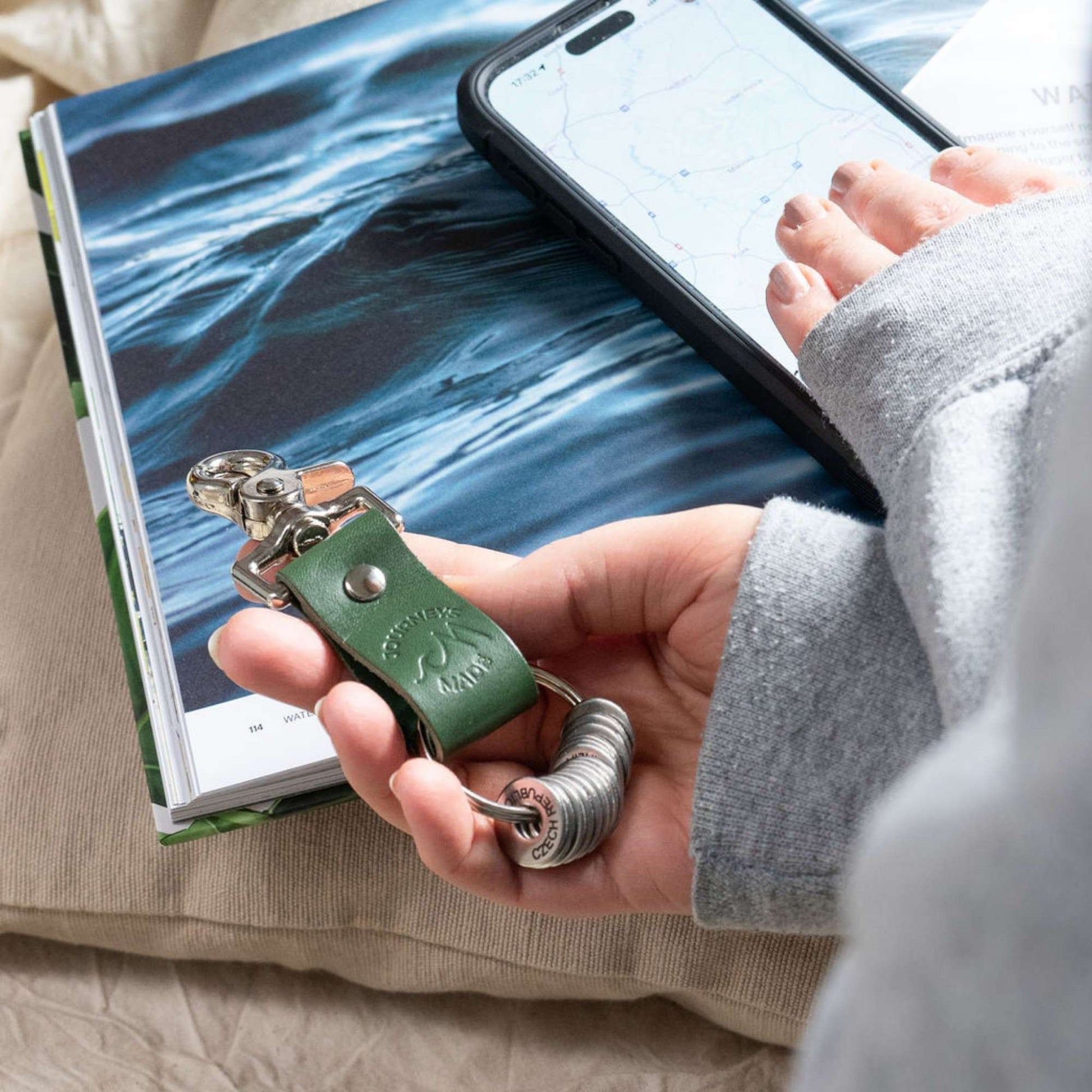 Person holding a green travel keyring with a phone and map, perfect for travel gifts.