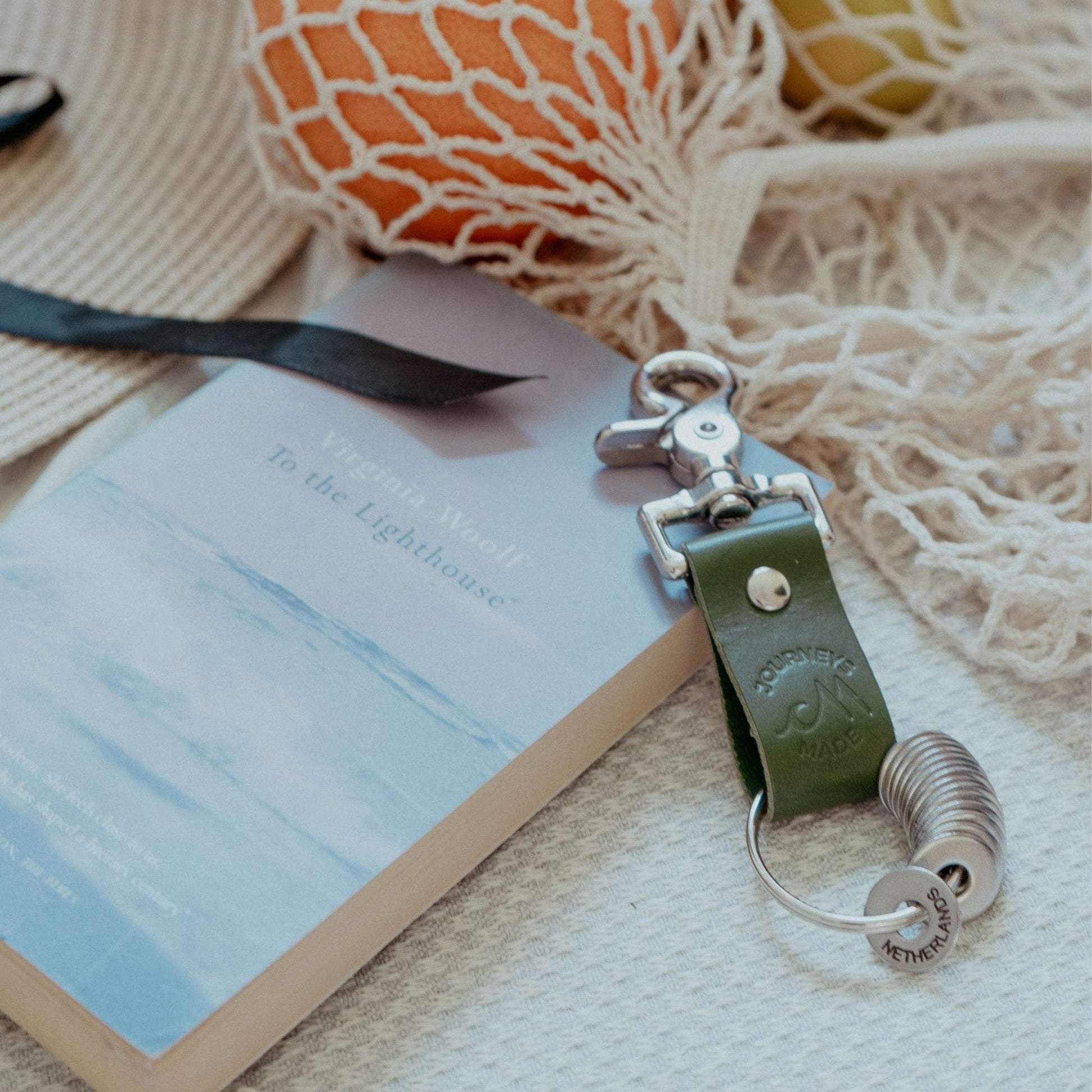Forest green leather travel keychain beside a book, perfect for travel gifts and keepsakes.