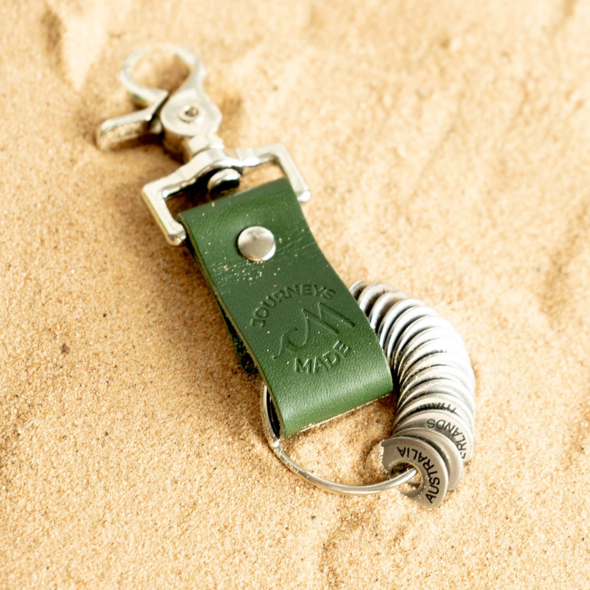 forest green travel gift with leather travel keyring and engraved travel tokens laying on a bed of golden sand