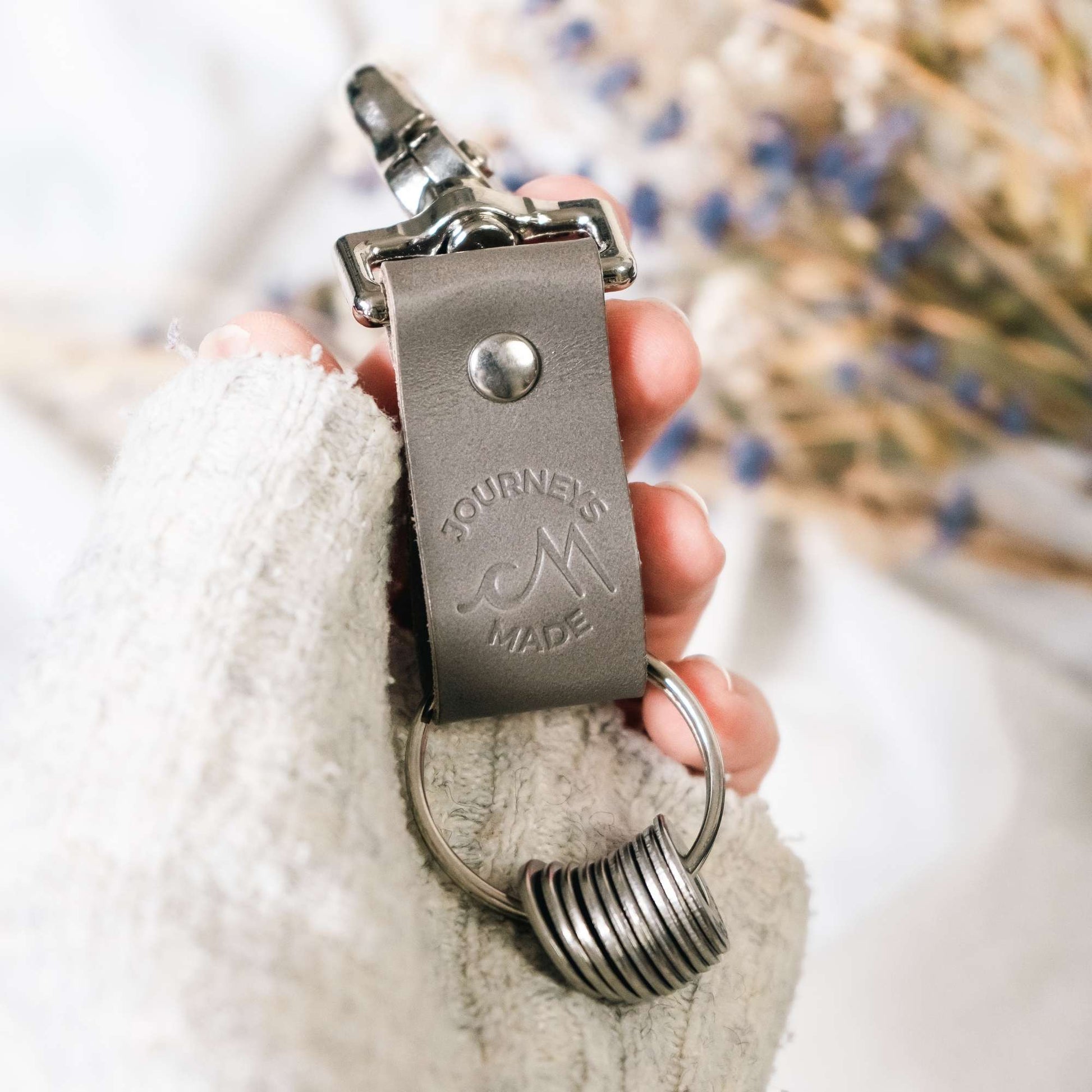 grey travel keyring as a gift being held in a white woman's hand wearing a white knitted jumper with dried lavender in the background