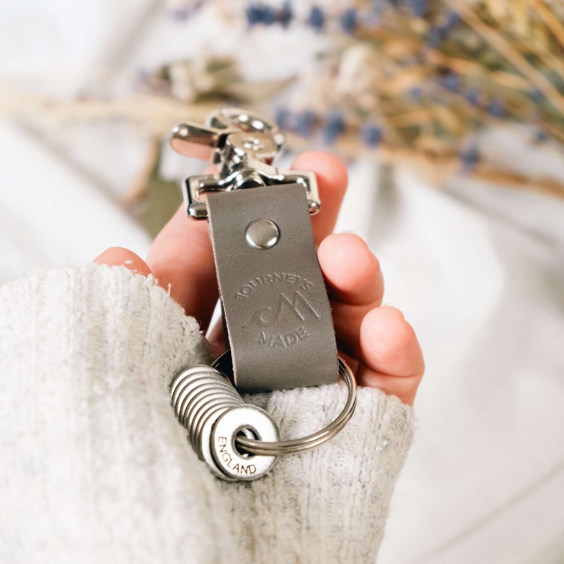 Handcrafted grey leather travel keyring with a destination token, perfect for travel gifts.