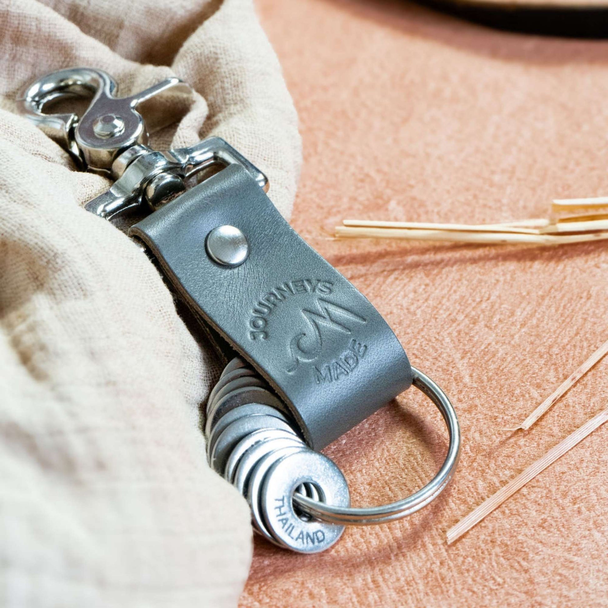 grey travel gift consisting of leather travel keyring and engraved travel tokens on the split ring, laying on a cream muslin and burnt orange background