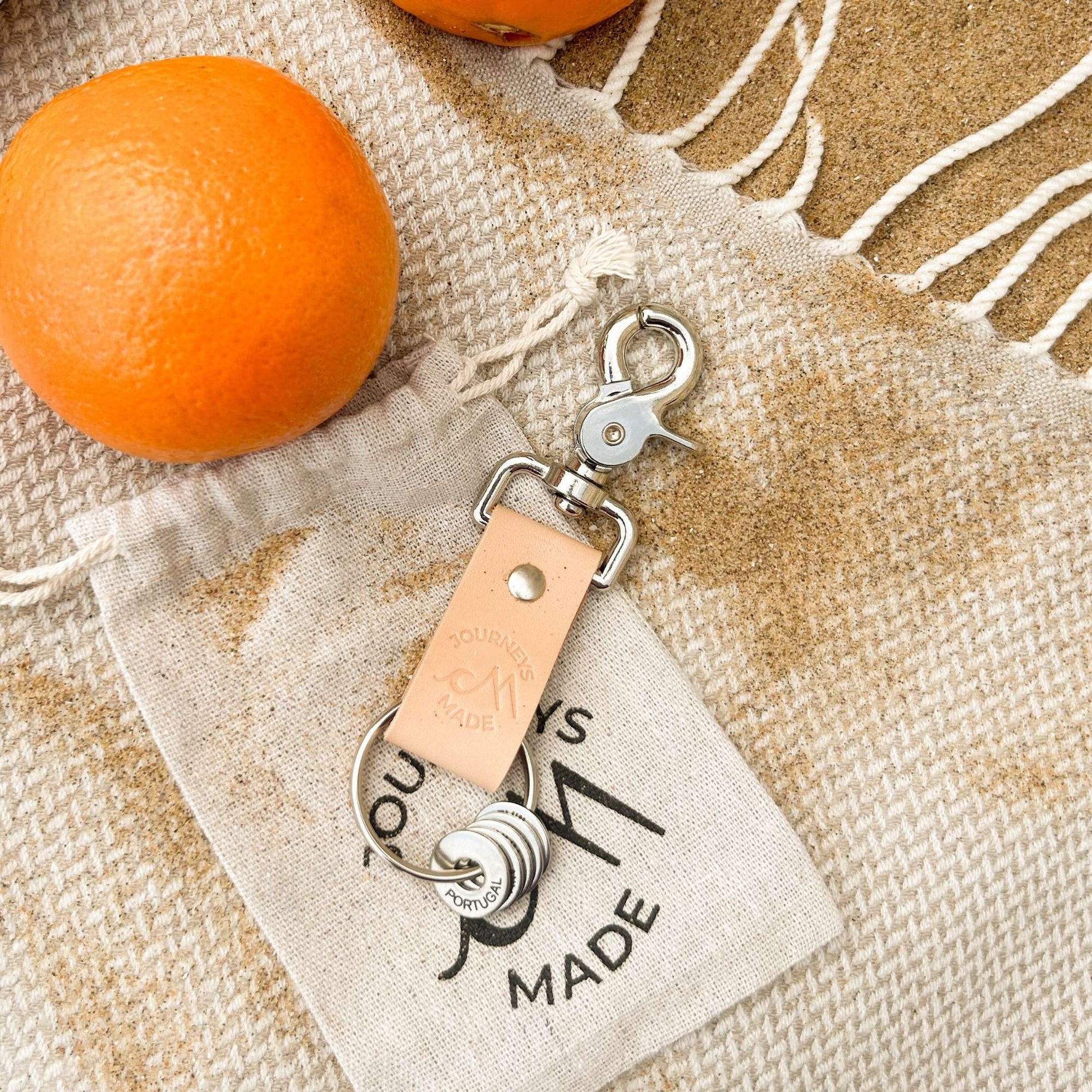 Natural travel keyring on a textured fabric background with oranges, perfect for travel gifts.