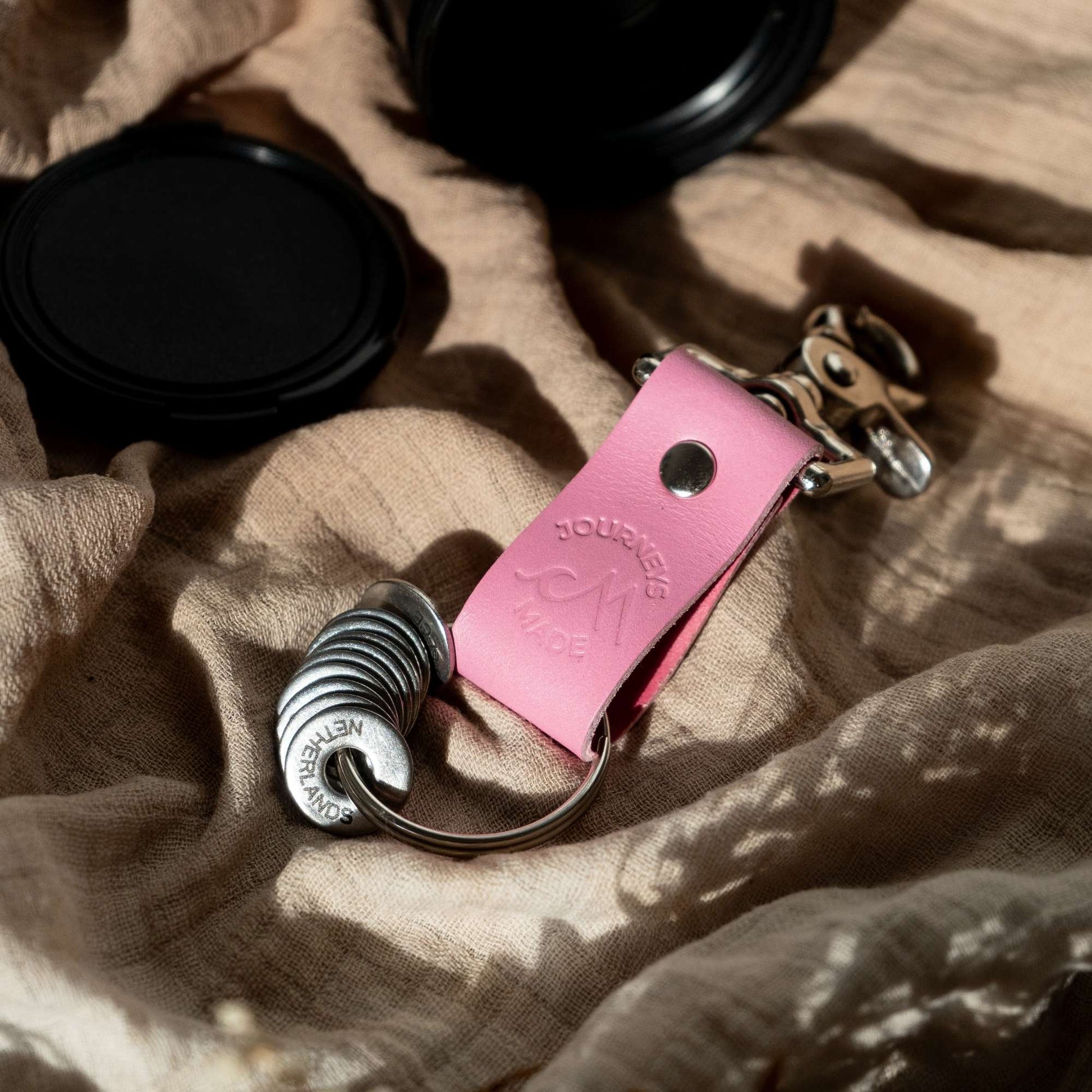 Pink leather travel keychain on fabric, part of a travel gift set celebrating journeys and memories.
