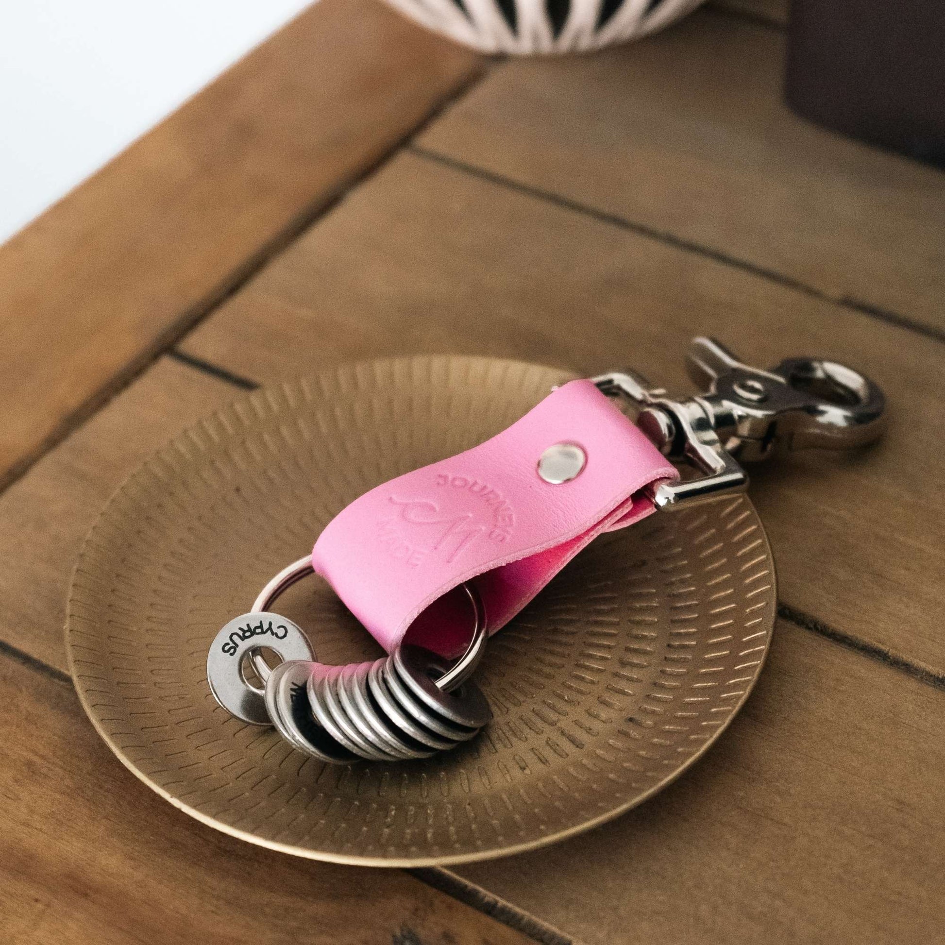 Pink leather travel keychain placed on a decorative gold plate, ideal for travel gifts and memorable journeys.