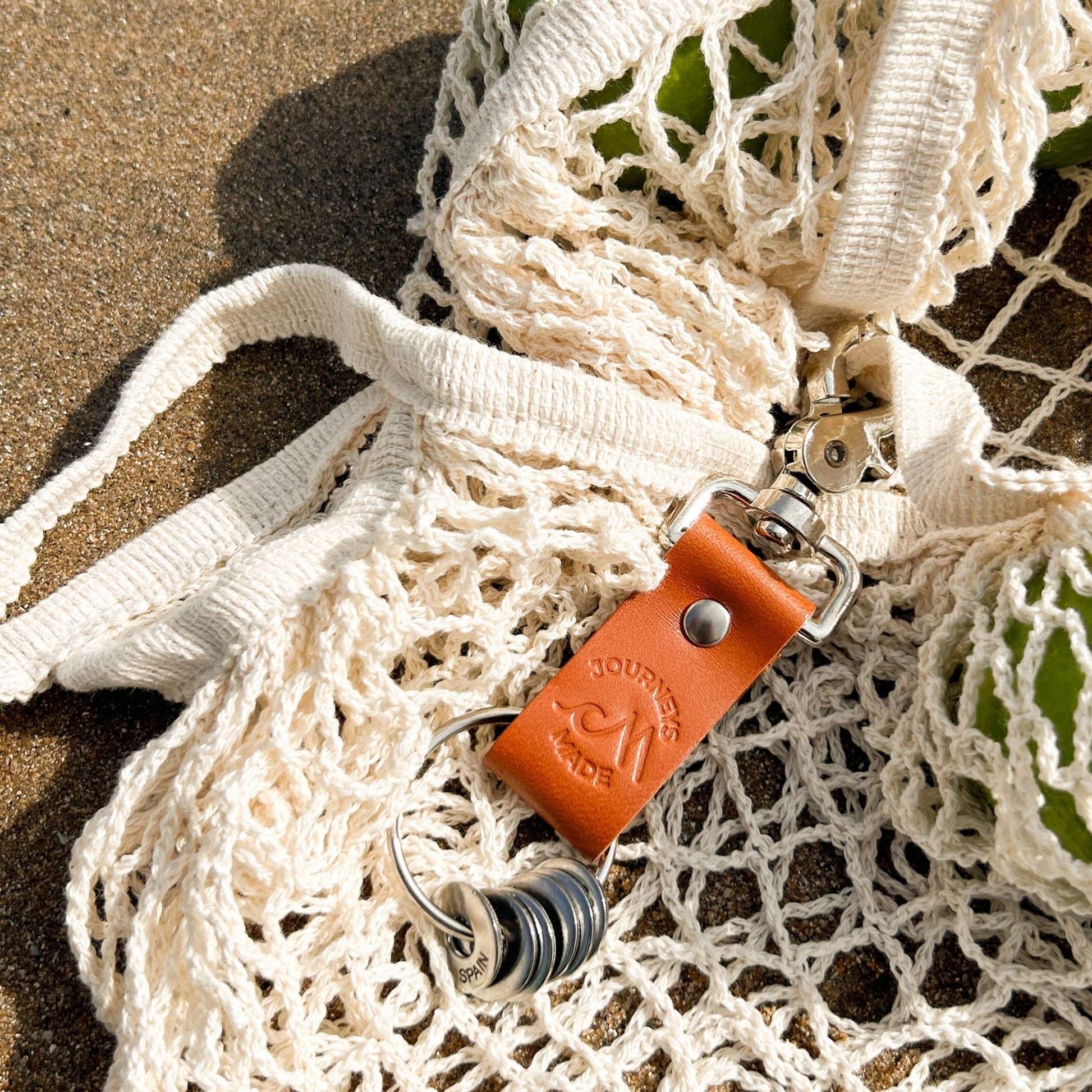 Tan leather travel keychain attached to a net bag, perfect for travel gifts and keepsakes.