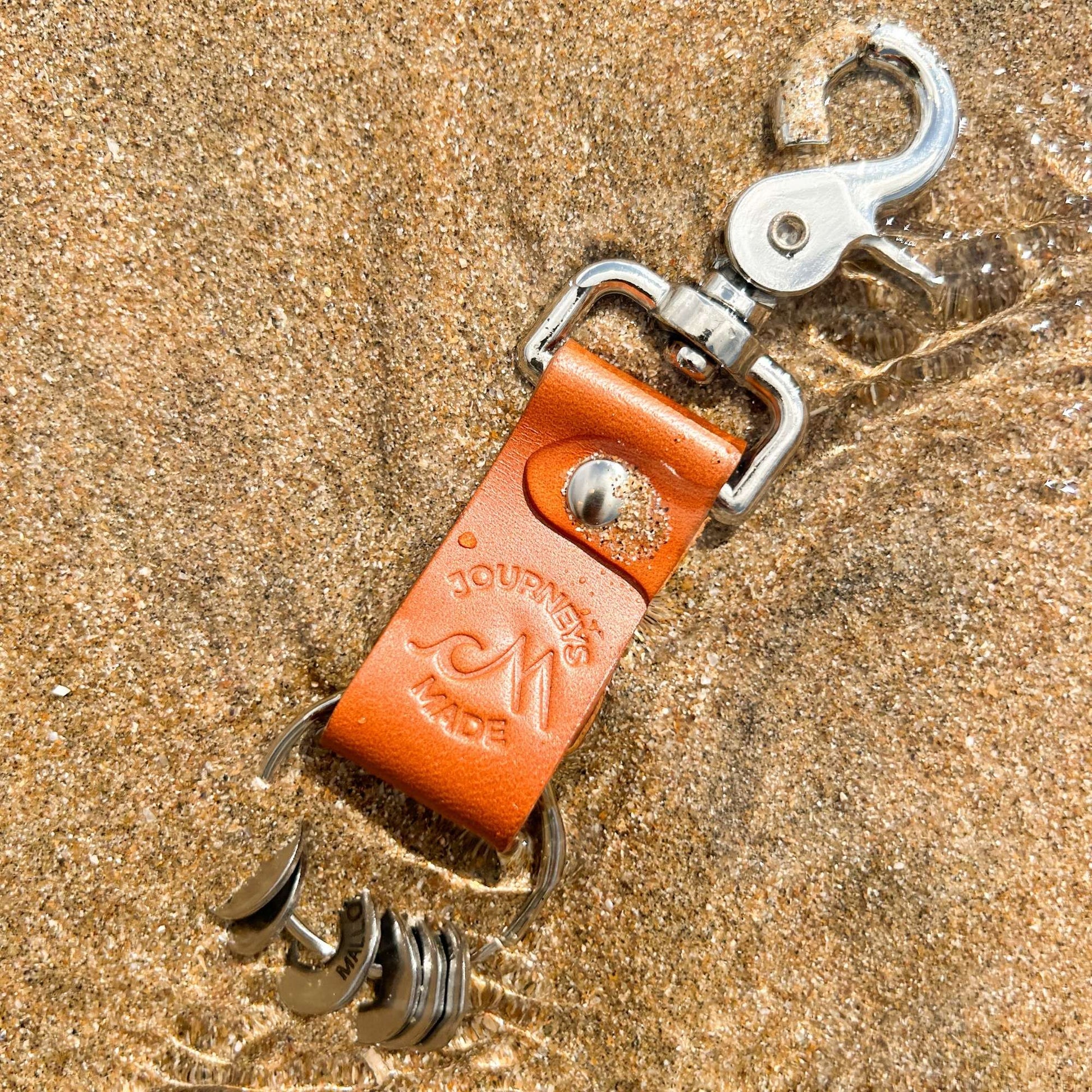 Tan leather travel keychain on sandy beach, part of a travel gift set for memorable journeys.