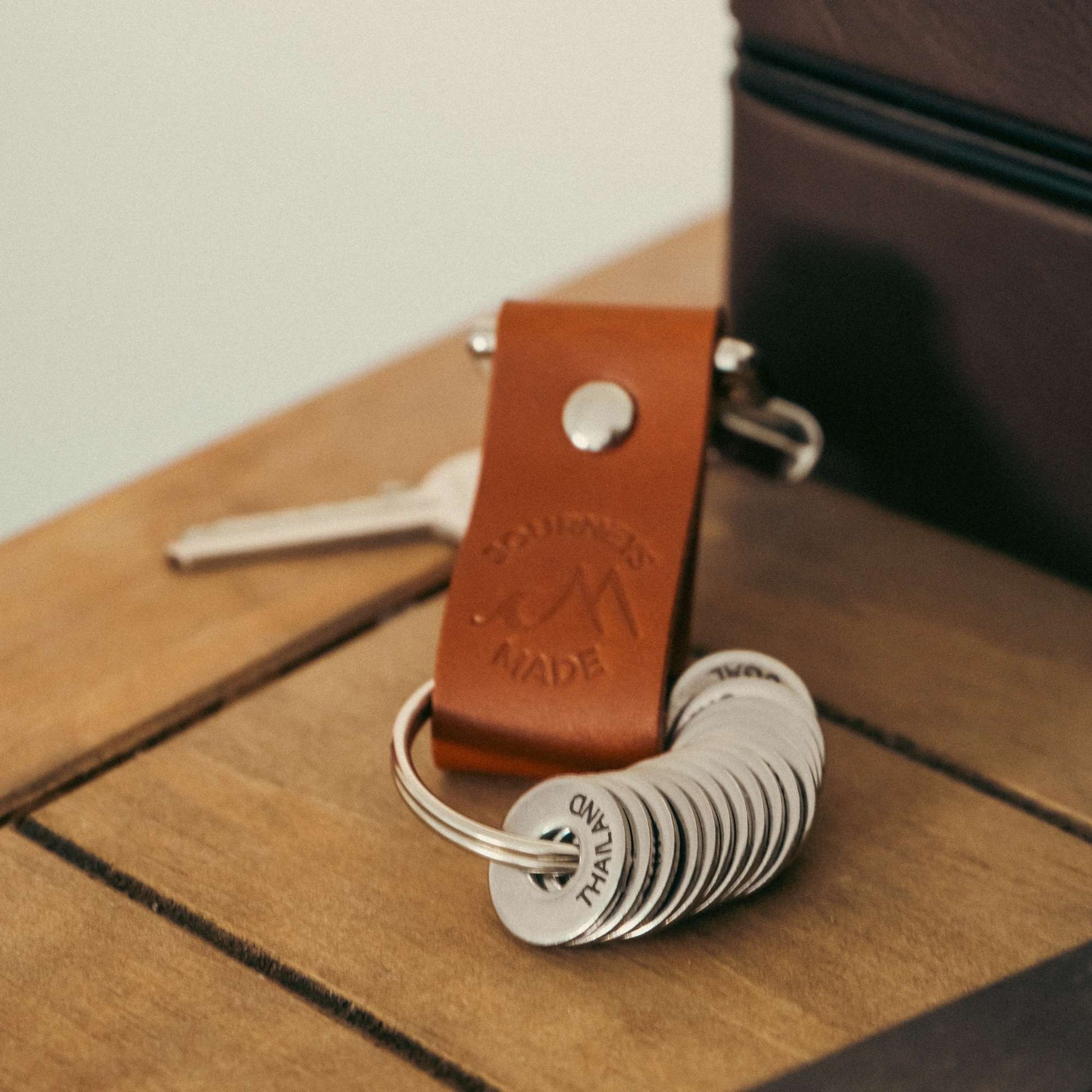 Tan leather travel keychain with engraved destination tokens, perfect for travelers and memorable journeys.