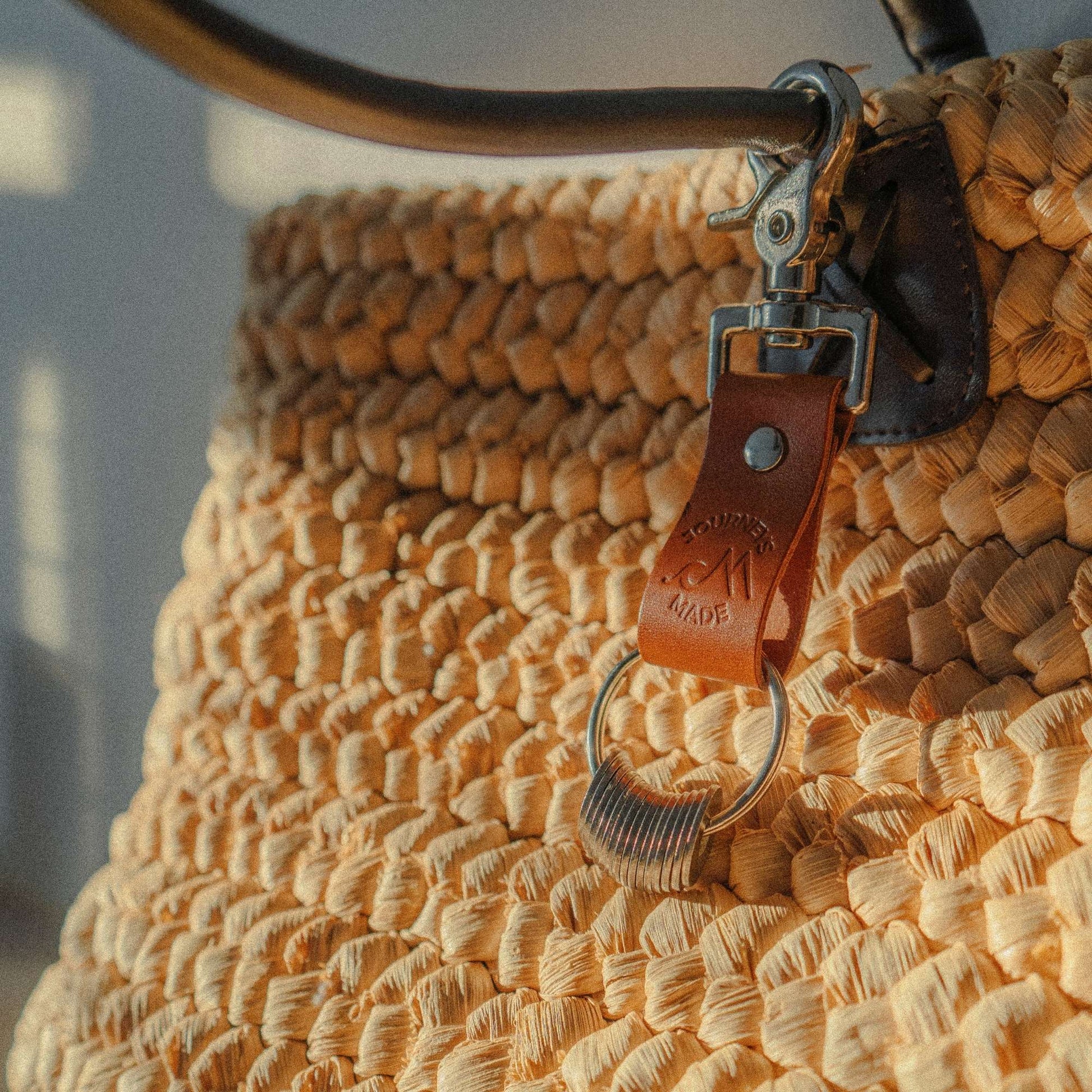 Close-up of a tan leather keychain attached to a woven straw bag, showcasing stylish travel accessories.