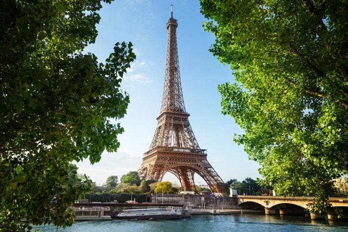 Eiffel Tower framed by green trees, overlooking the Seine River in Paris, France.