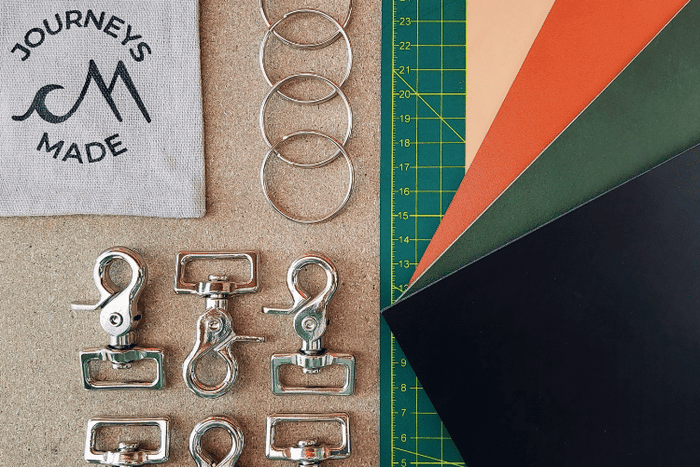 Crafting materials for Journeys Made travel keyrings, including metal clips, rings, and colorful sheets.
