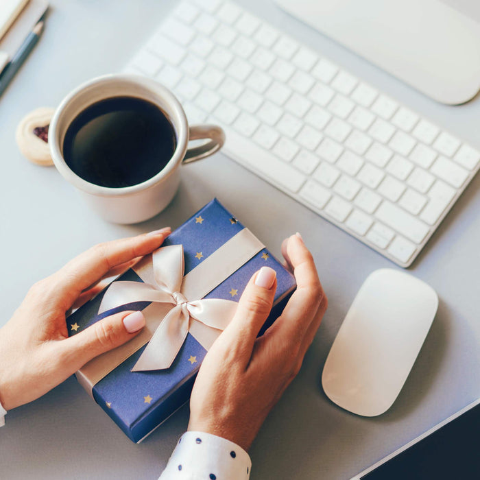 white woman with her hands on a blue wrapped gift sitting at a grey desk