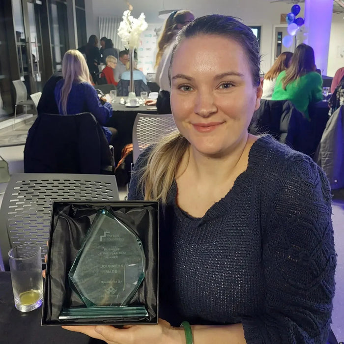 Jade Scammells founder of Journeys Made wearing a blue knitted dress holding a glass trophy for Business of the Year at the Kent Foundation Awards 2023.