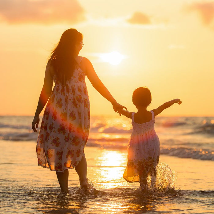 mother and daughter walking on the beach holding hands at sunset