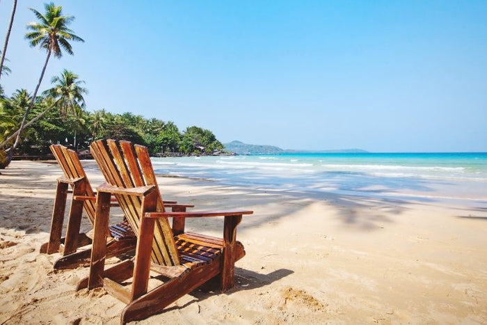 Relaxing beach scene with wooden chairs, palm trees, and a peaceful ocean view perfect for summer travel.