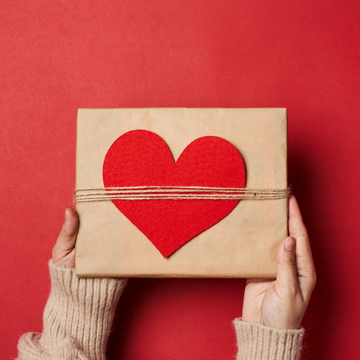 white woman in a knitted jumper holding a kraft box with a red love heart cut out and tied on for Valentine's Day