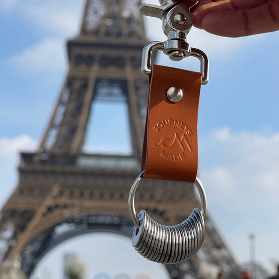 Travel keyring featuring a leather strap and metal coil, with the Eiffel Tower in the background, perfect for travel gifts.