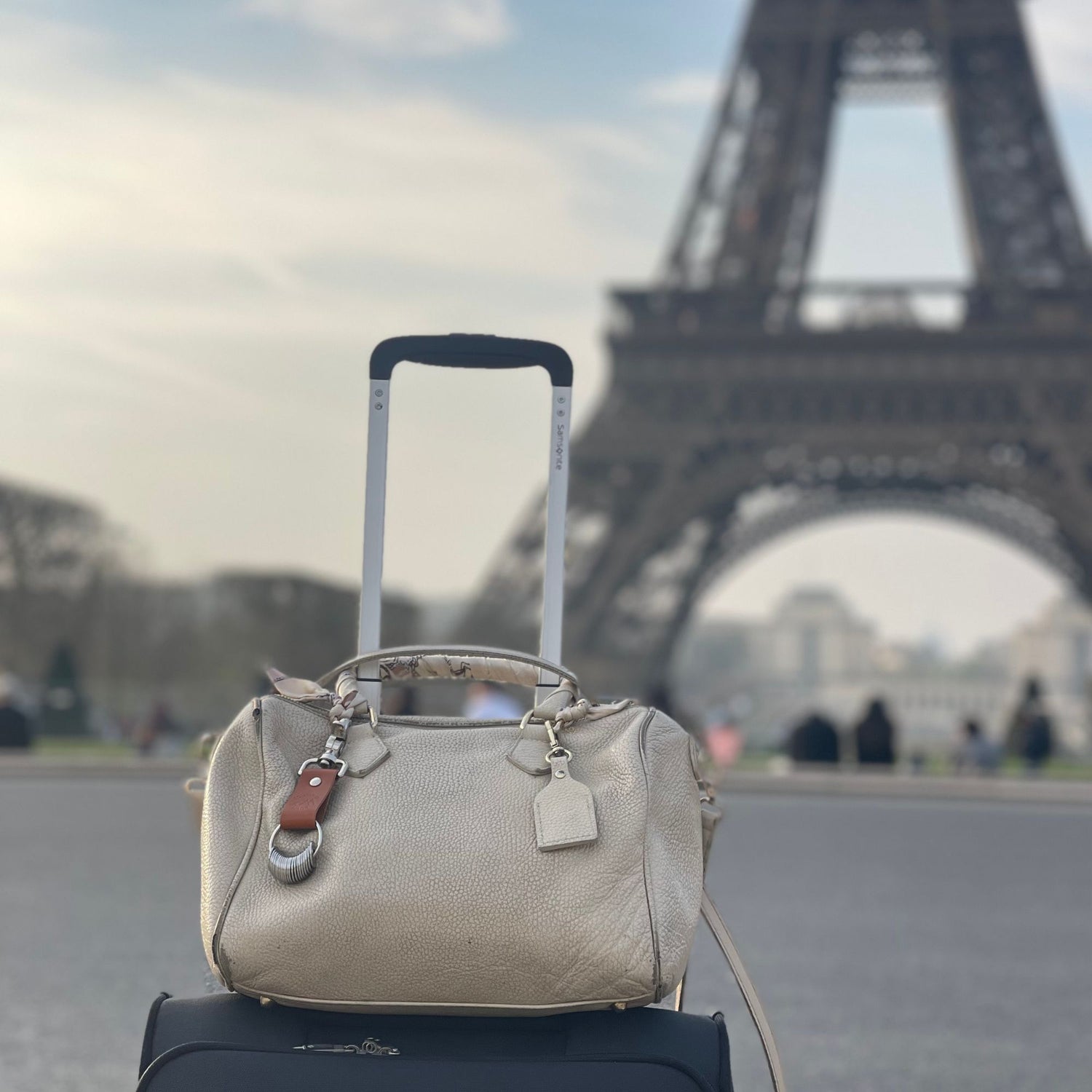 Stylish handbag on a suitcase in front of the Eiffel Tower, perfect for travel gifts.