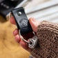 black travel gift with leather travel keyring and engraved travel tokens being held by a white woman wearing a brown knitted jumper with a white-washed wooden board in the background