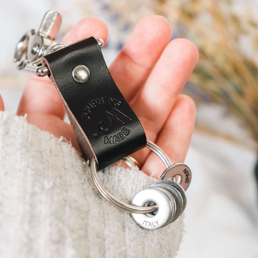 dark brown travel gift consisting of leather travel keyring and engraved travel tokens on the split ring being held by white woman wearing a cream jumper and dried lavender in the background
