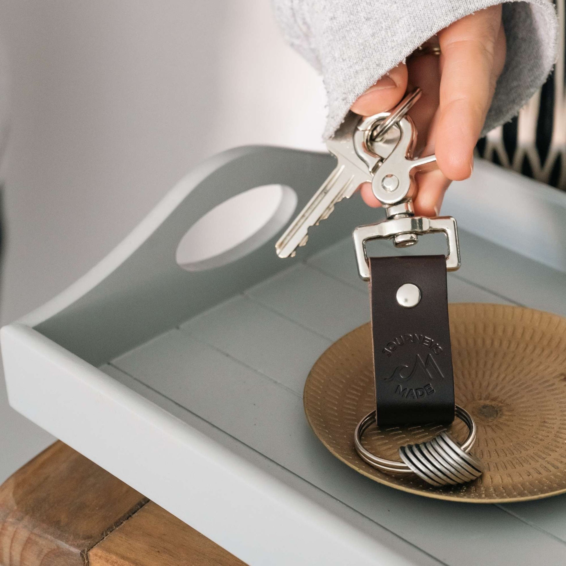 User holding a stylish travel keyring with keys, displayed on a wooden tray and plate.