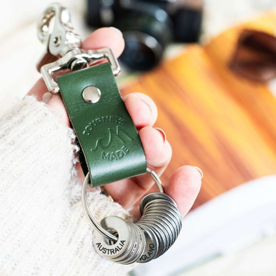 forest green travel gift with leather travel keyring and engraved travel tokens, with token showing as Australia, being held by white woman wearing a white jumper