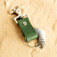 forest green travel gift with leather travel keyring and engraved travel tokens laying on a bed of golden sand