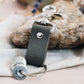 grey travel gift consisting of leather travel keyring and engraved travel tokens on the split ring, leaning against a rock