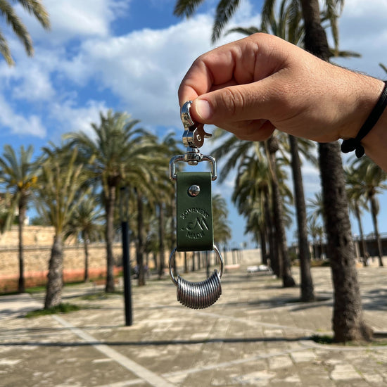 Hand holding a green travel keyring, surrounded by palm trees, ideal for travel gifts.