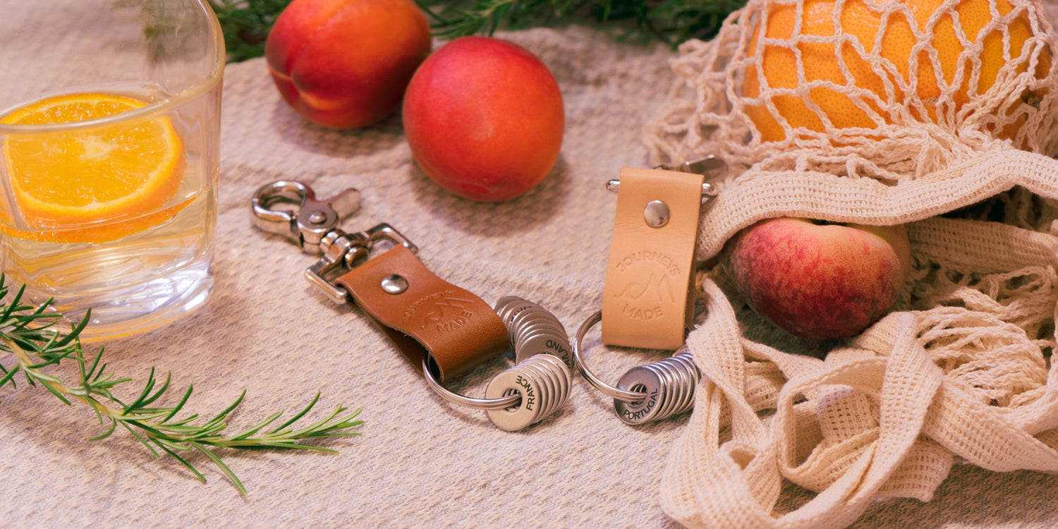 Stylish travel keyring and leather keychain on a natural fabric with fruits and glass of orange drink.